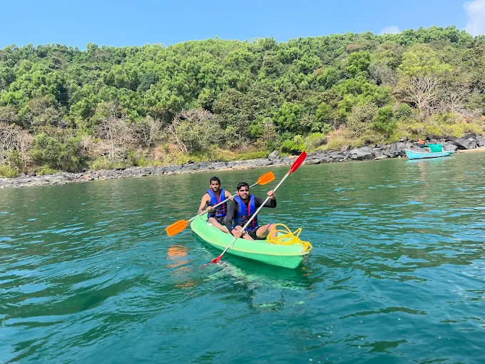 Two guests paddling a green kayak in a sheltered bay below forested hills